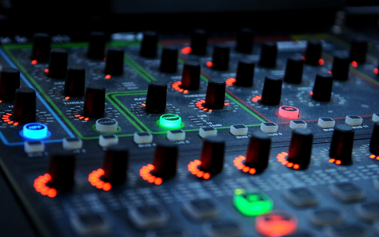 Close-up of a mixing desk with glowing coral, green and blue buttons.